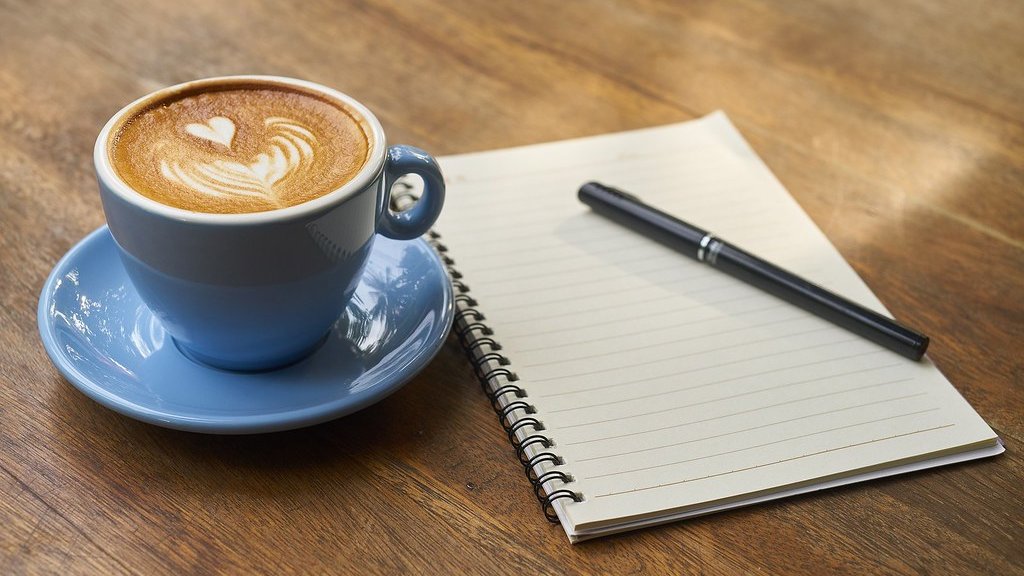 木の机に置いたコーヒーとノート